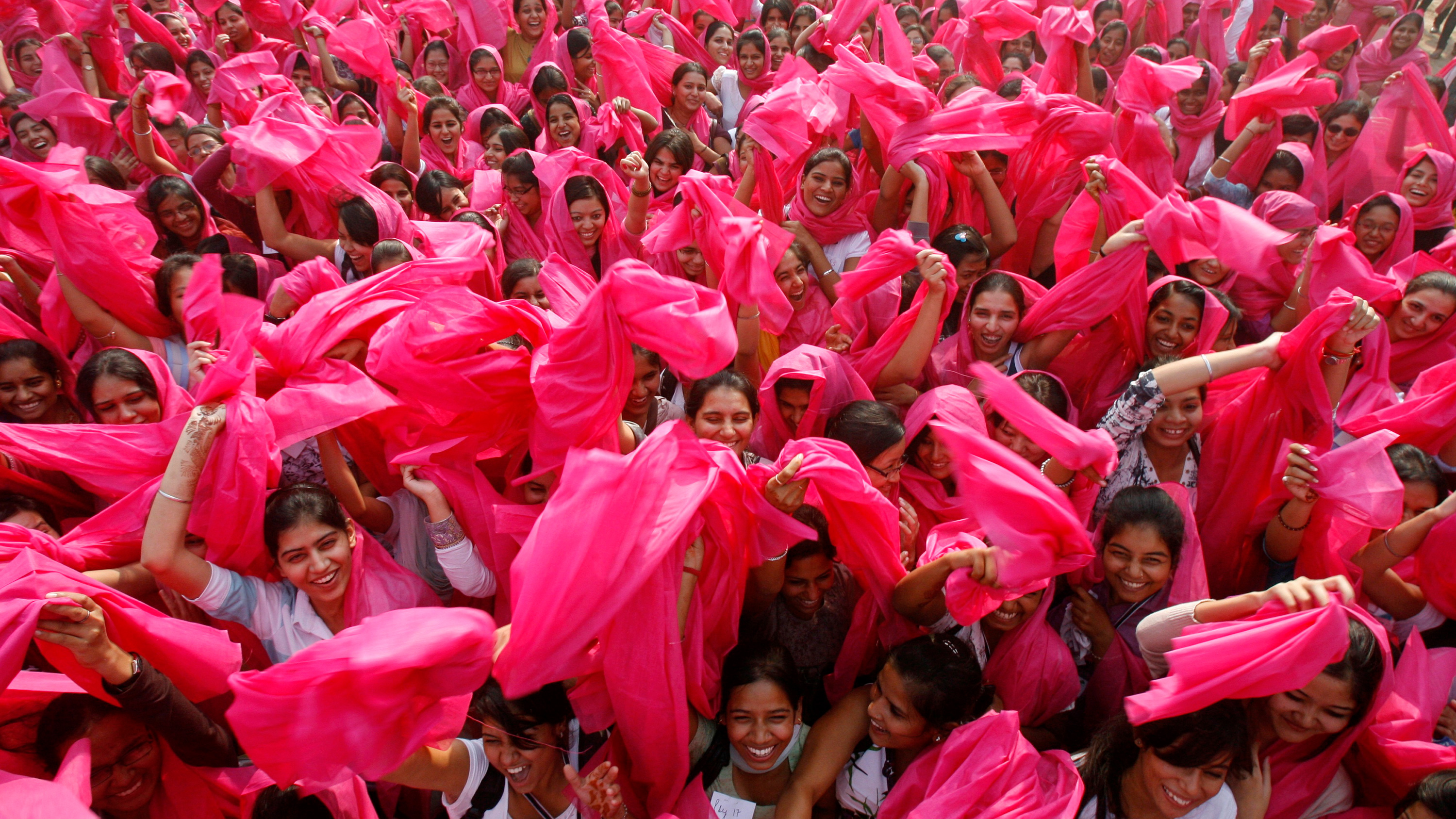 The photo shows a large crowd of women waving pink scarves.