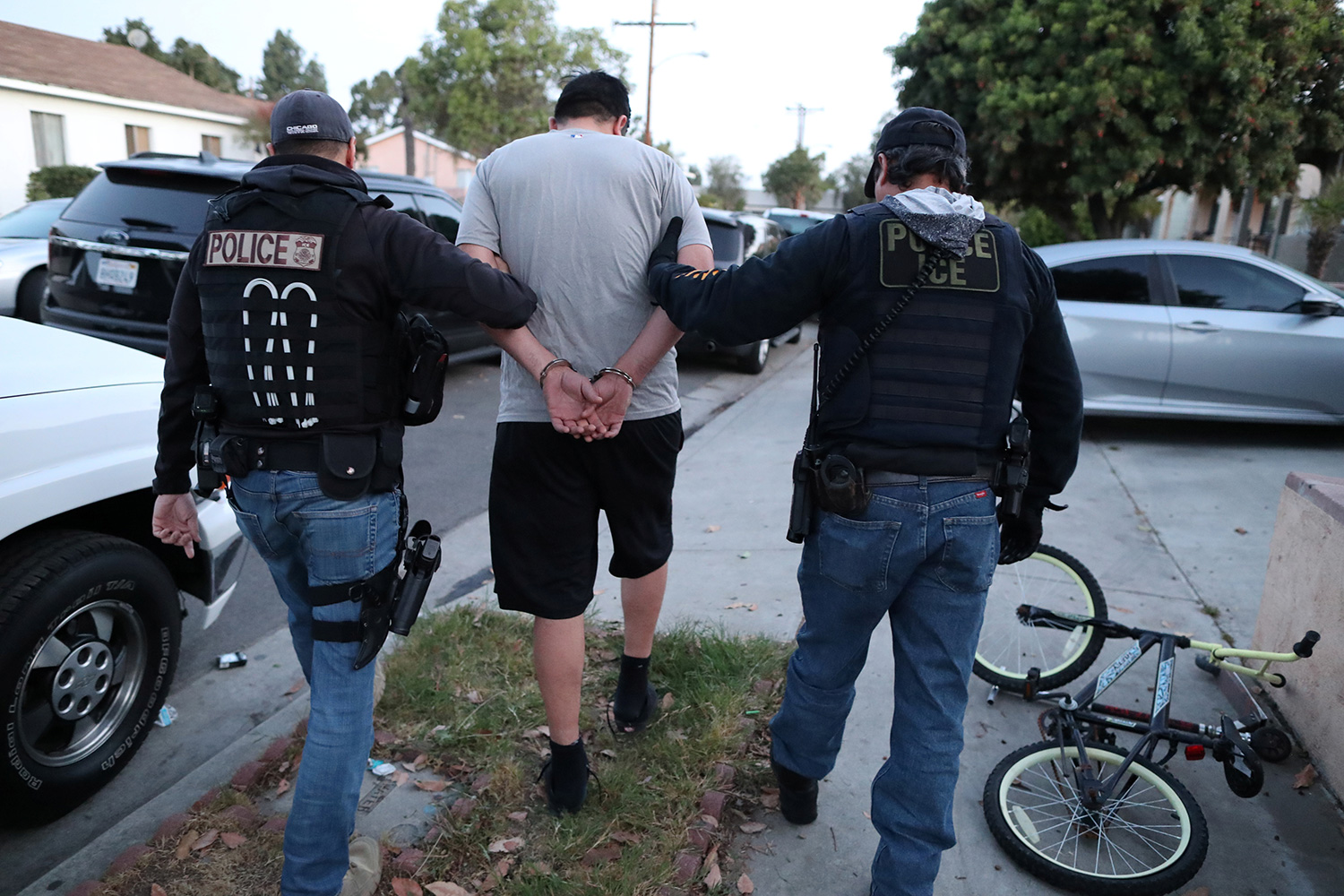 The photo shows two officers leading a person away from the camera in handcuffs.