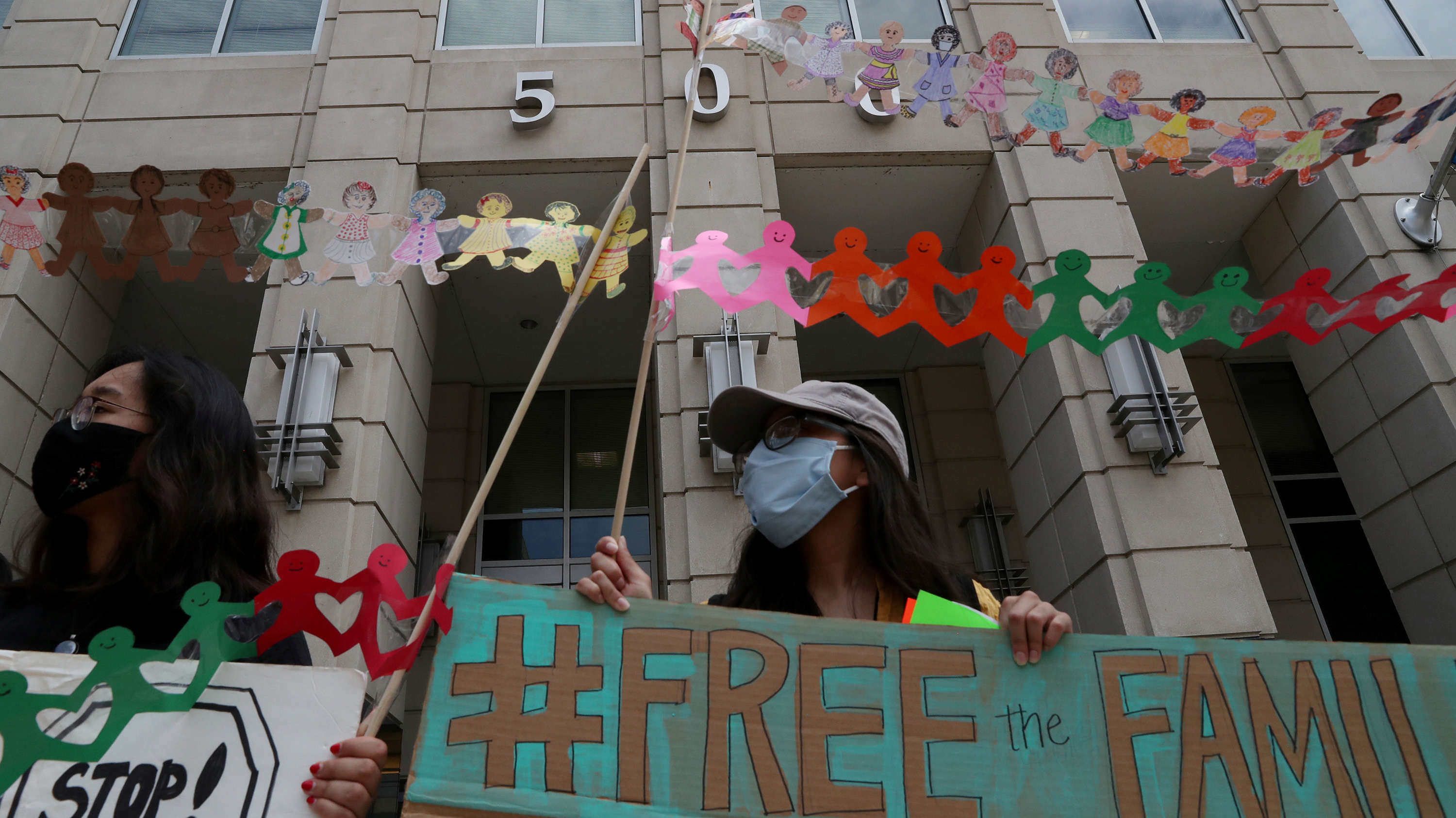 The photo shows a protester wearing a mask and holding a sign that "#FREE THE FAMILY."