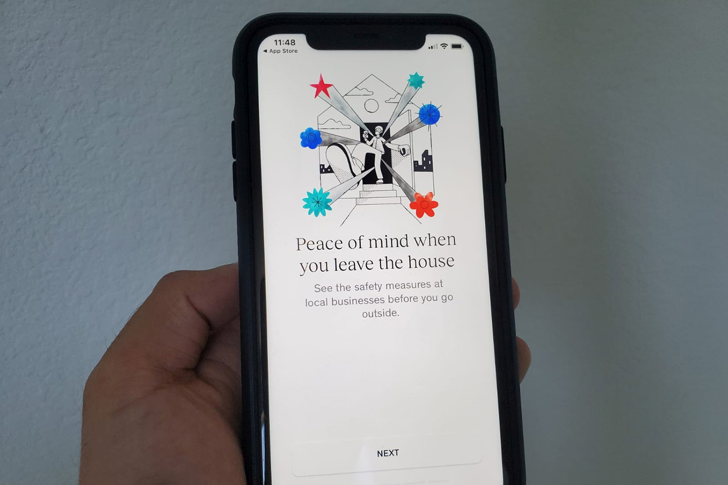 The photo shows a hand holding an iPhone on which is displayed the app menu page,