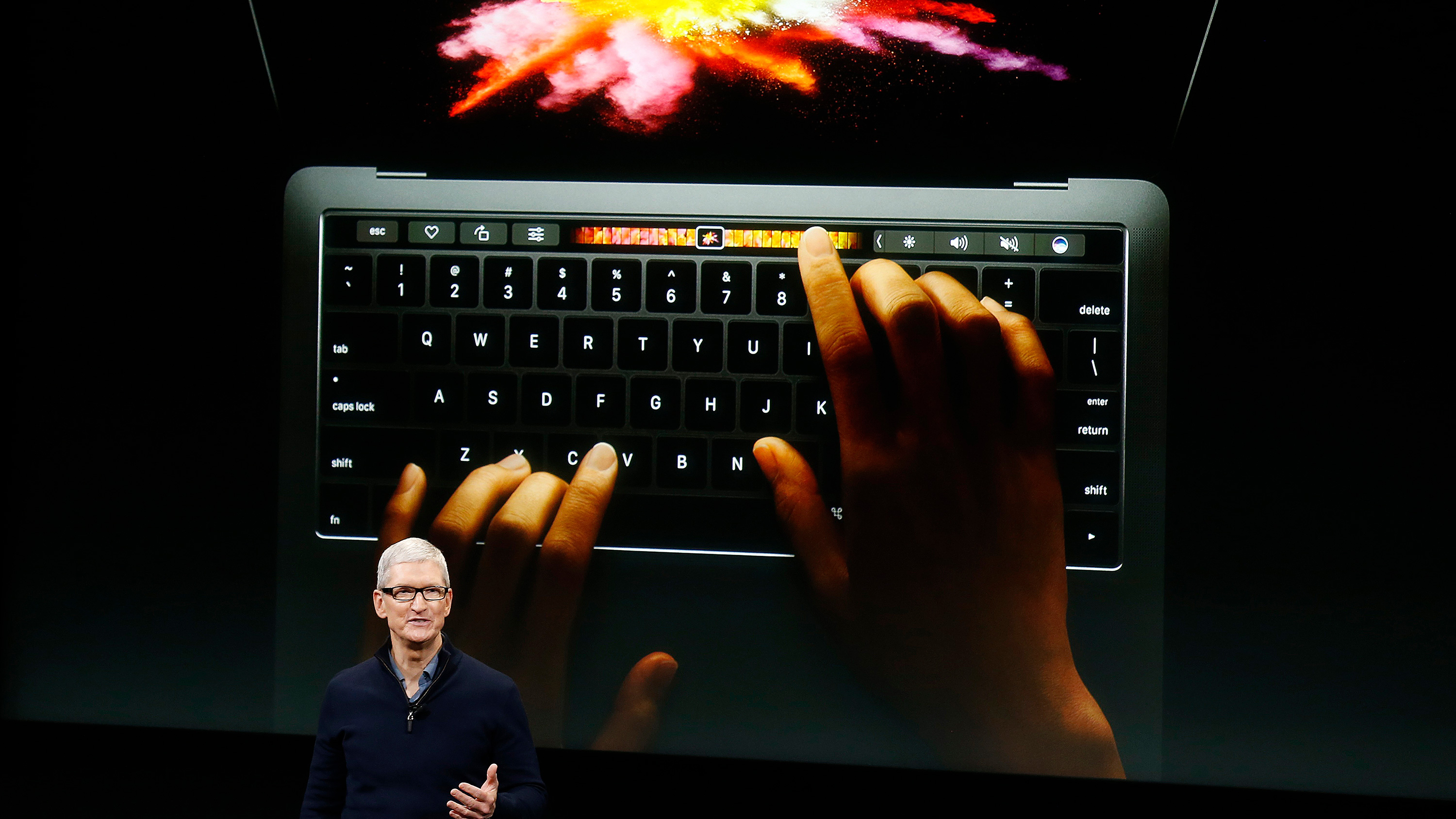 The photo shows Cook standing in front of a huge display screen giving a talk at a launch event.