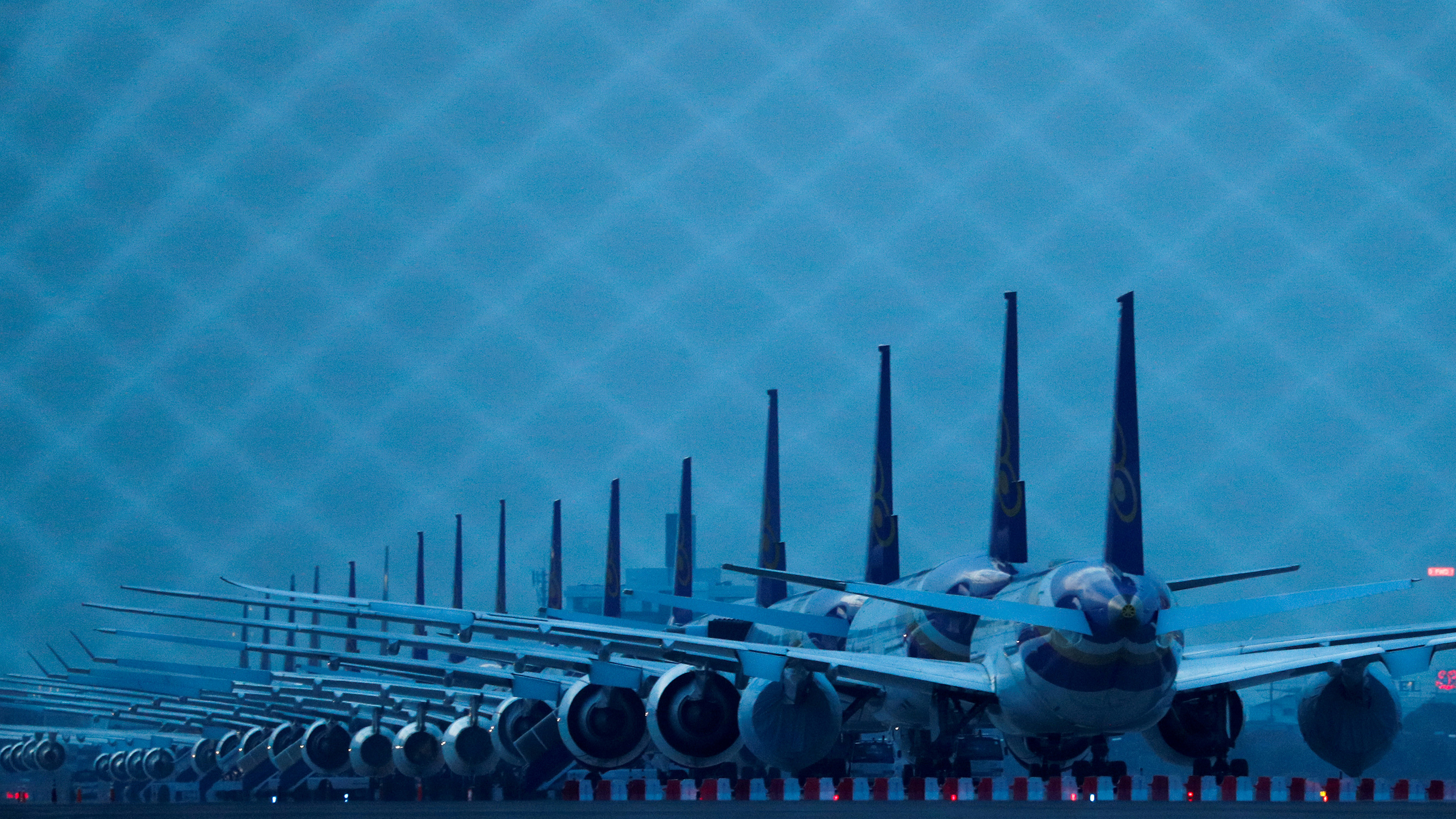 The photo shows a row of airplanes at dusk in a dark blue light.