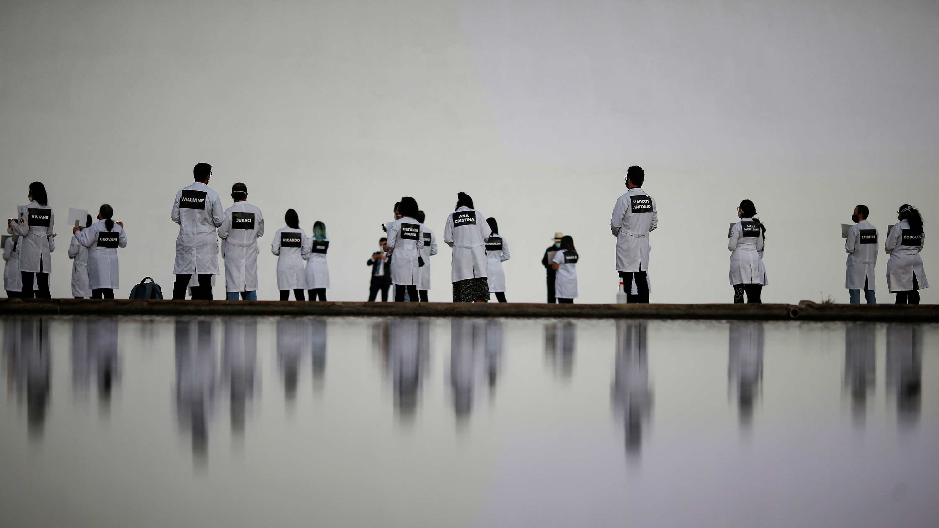 The image showsa bunch of people wearing white nurses' uniforms standing in the distance by a reflecting pool.