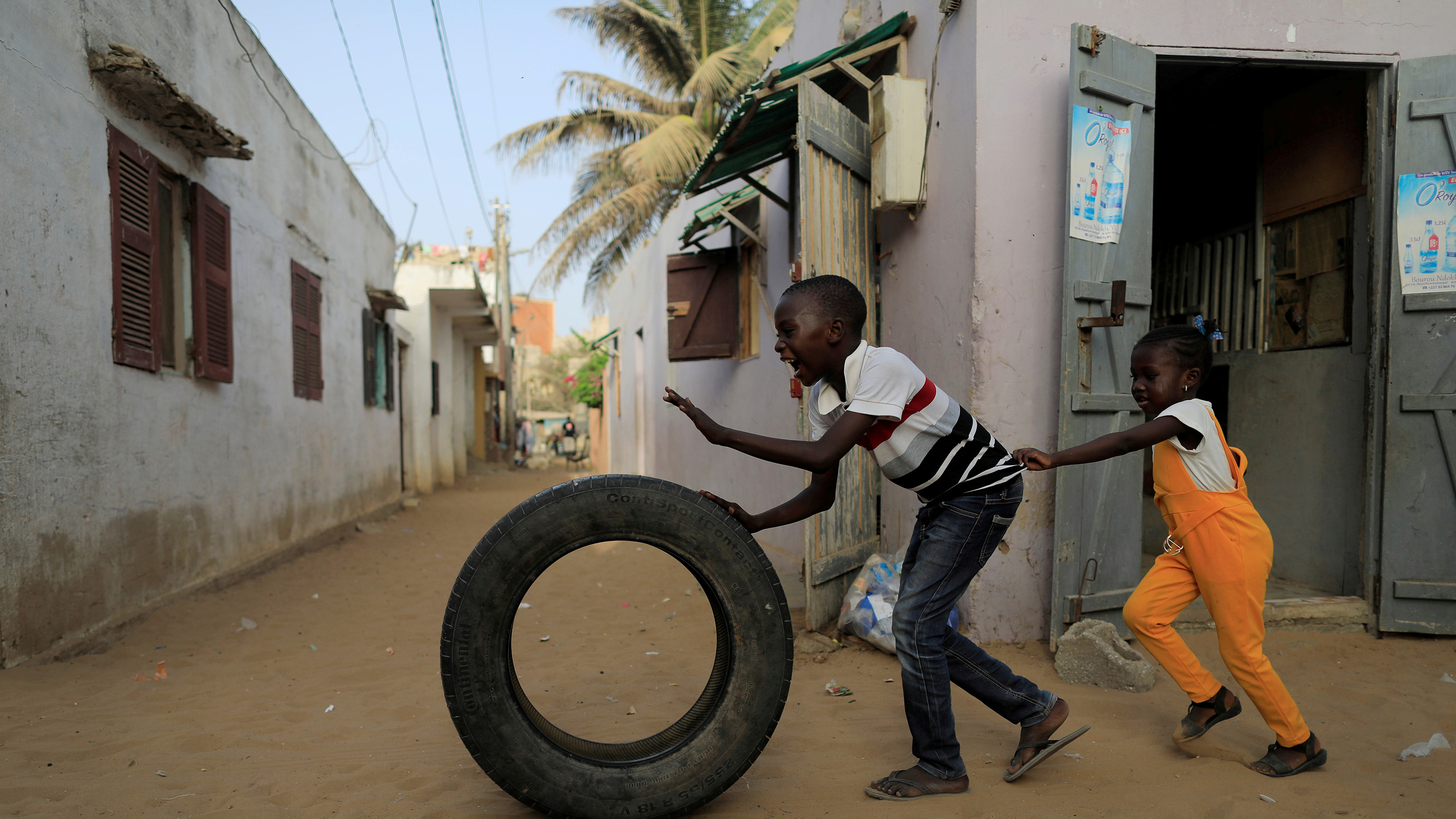 The image shows a boy and girl chasing a tire.