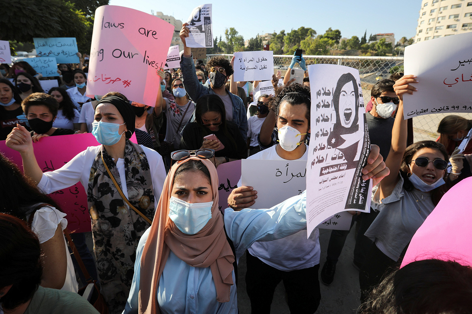 The photo shows a large crowd of protesters wearing masks and holding signs.