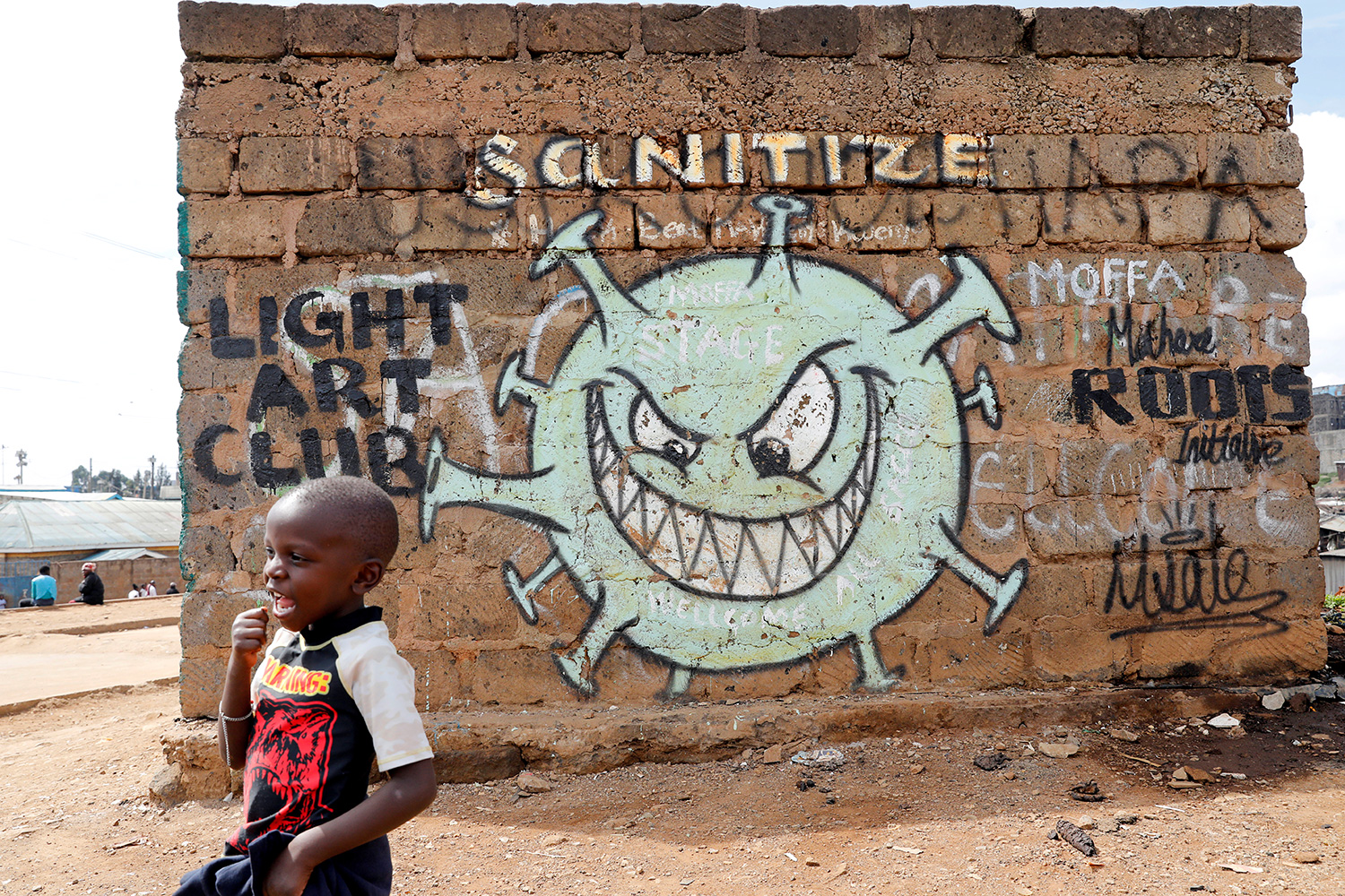 The photo shows a young boy in front of a wall decorated with a huge graffiti of a coronavirus.