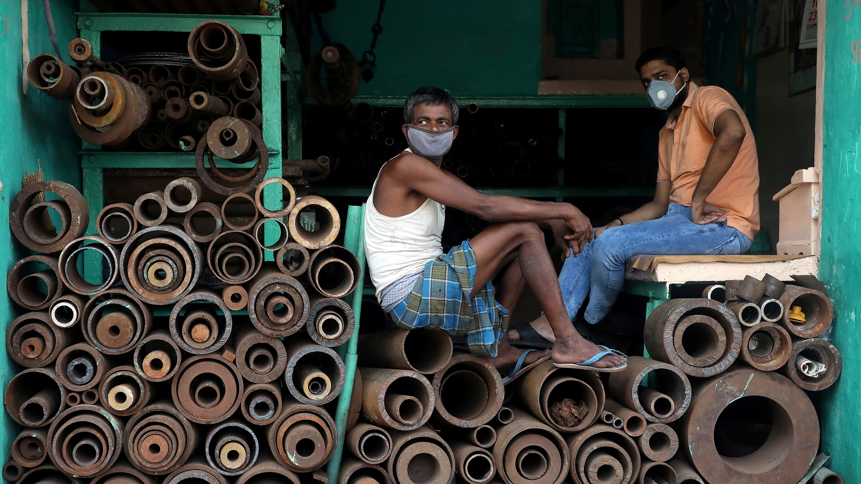This is a striking photo with two men sitting on stacked metal pipes wearing masks.