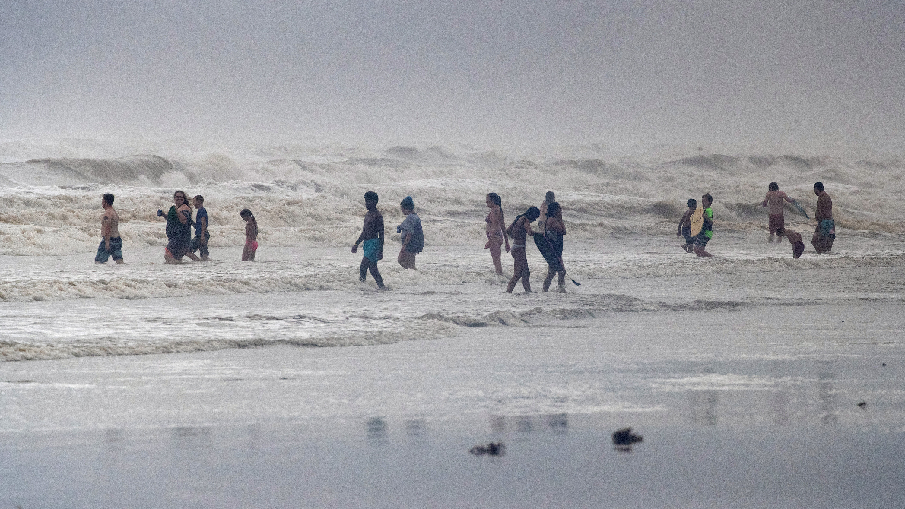 The photo shows a number of people on a beach amid huge waves.