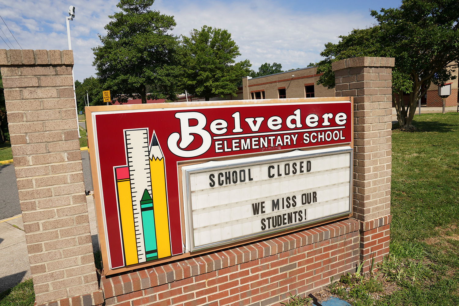 The photo shows an elementary school with a sign out front that reads, "School Closed / We miss our students."