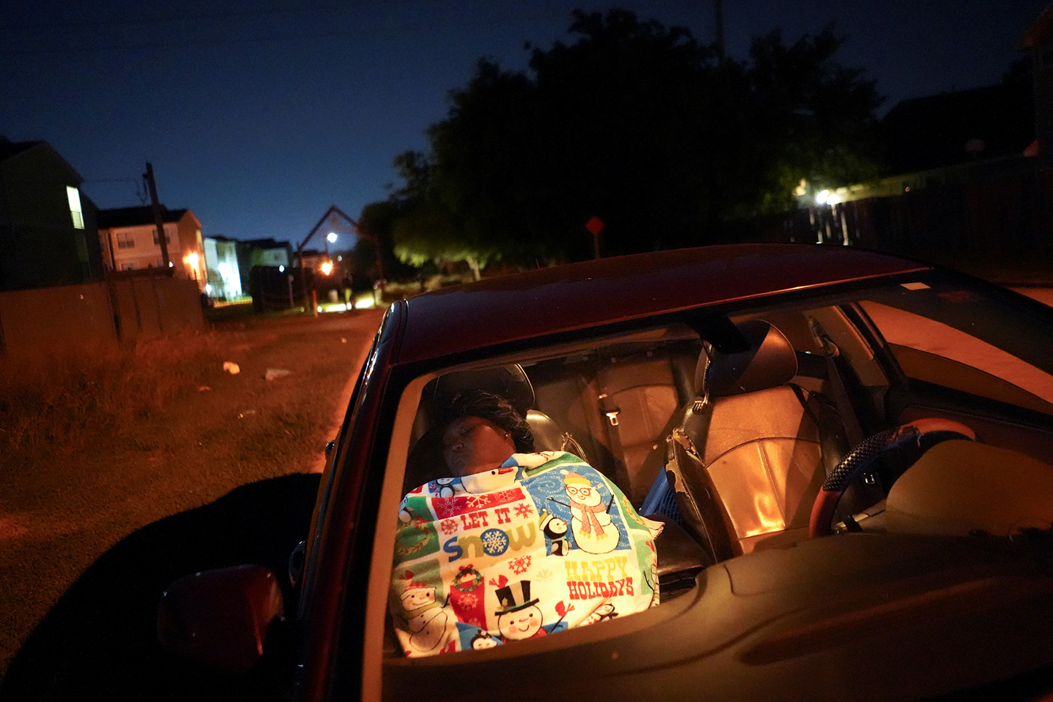 Picture shows the woman reclined in the passenger seat of her car at night. The glow from her phone illuminates her face.