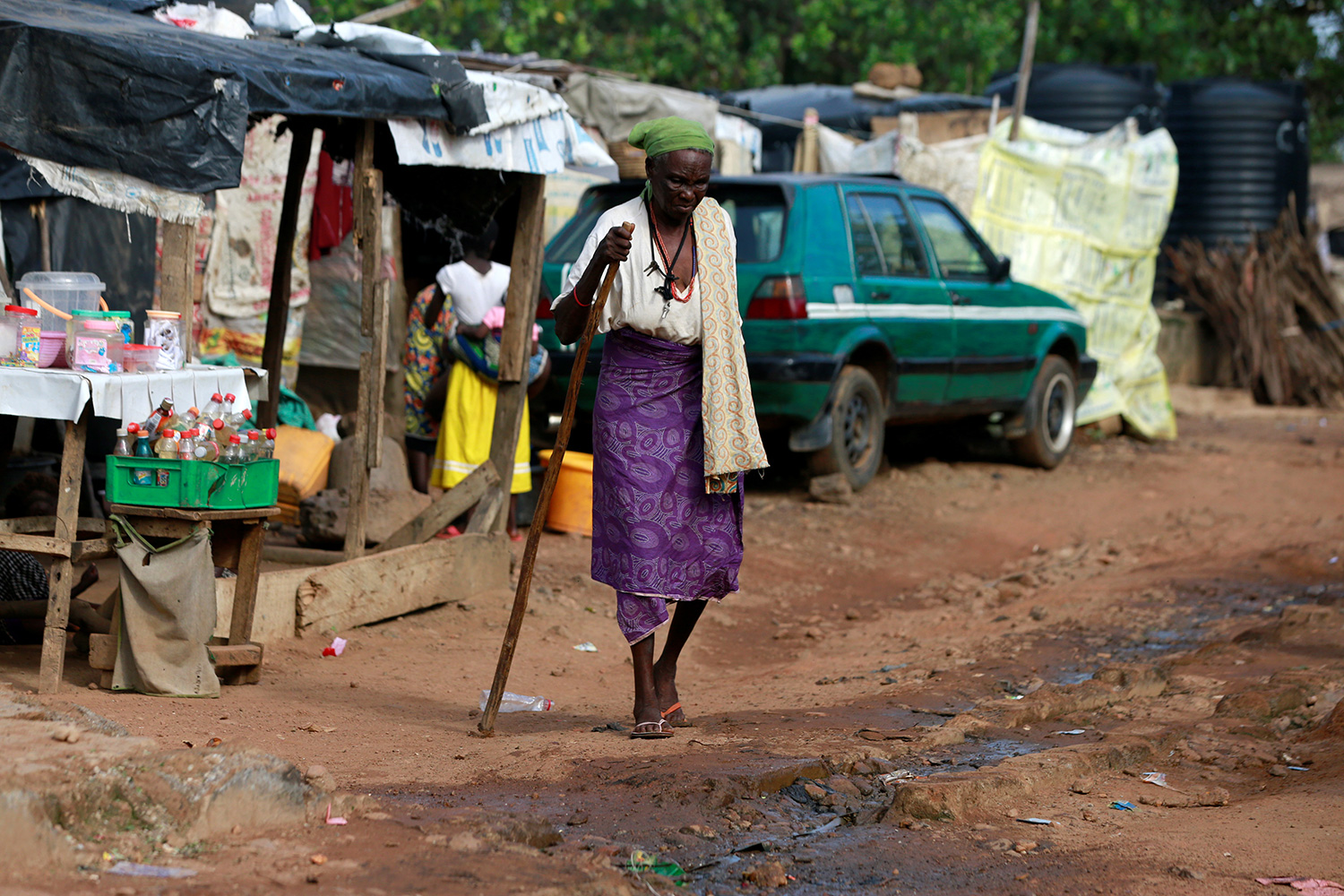 The photo shows the older woman walking along a muddy unpaved road.