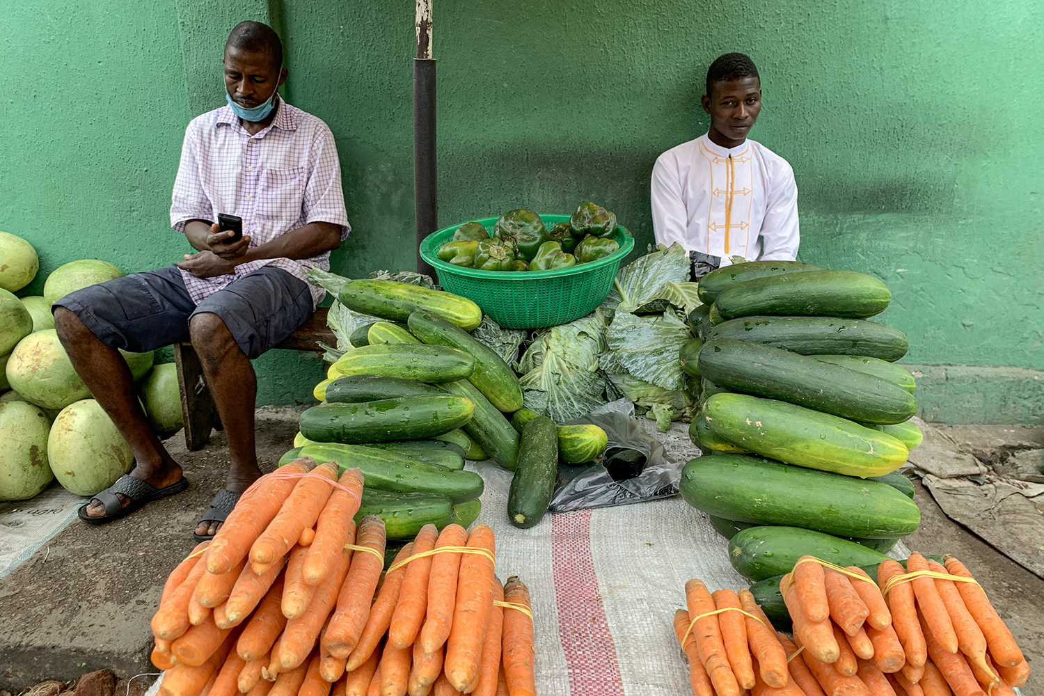 The photo shows two men amid carots, melons, zucchini and other fresh foods.