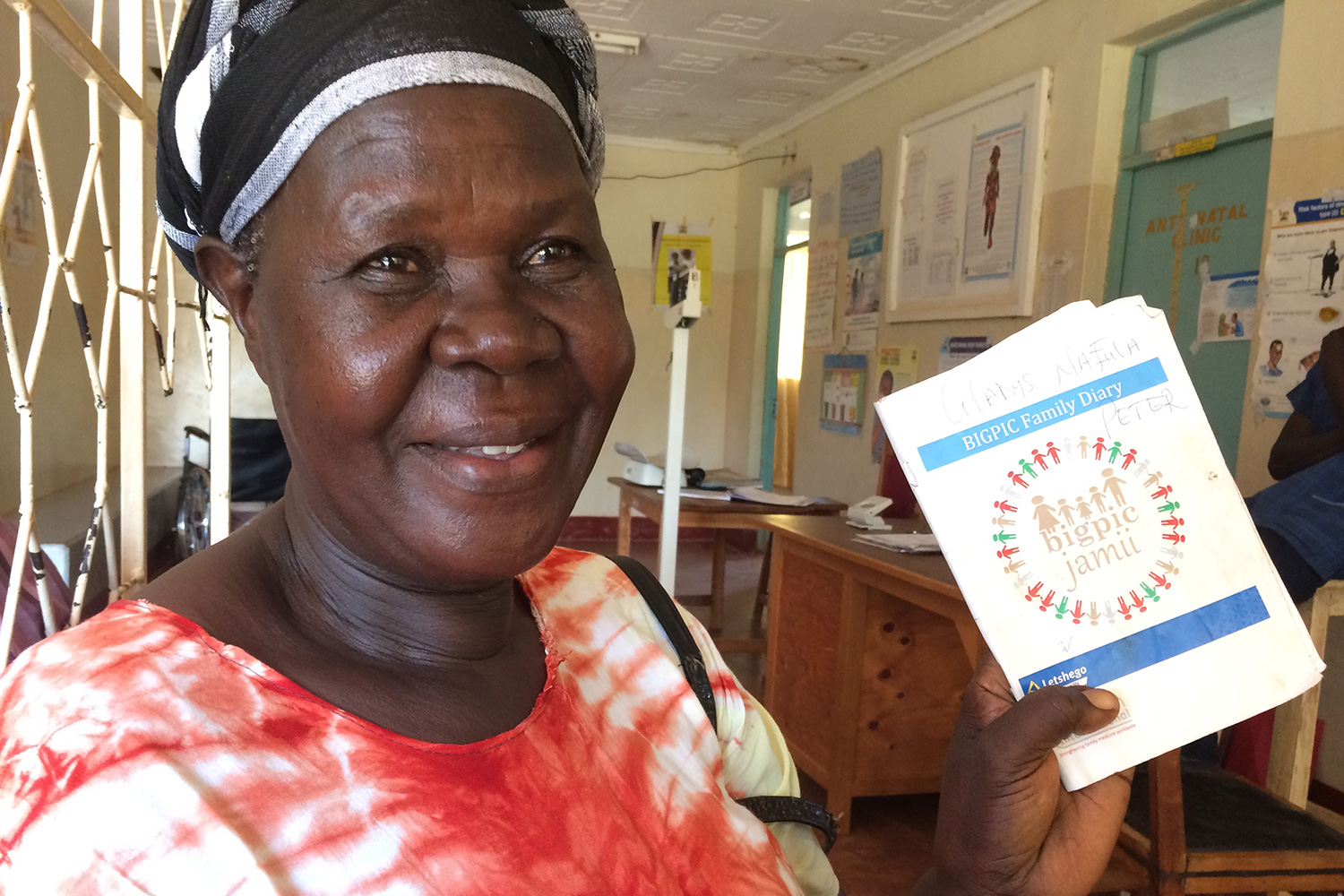 The image shows the interior of a clinic with a woman holding up information brochures.