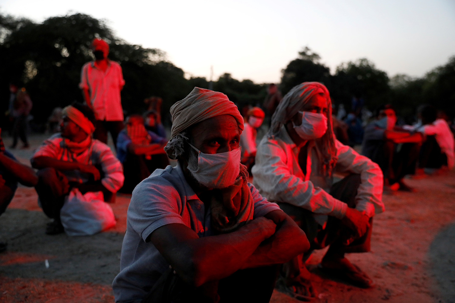 This is an eerie and haunting photo with several people sitting on the ground in an outdoor location in low lighting. They are bathed in a dark red light.