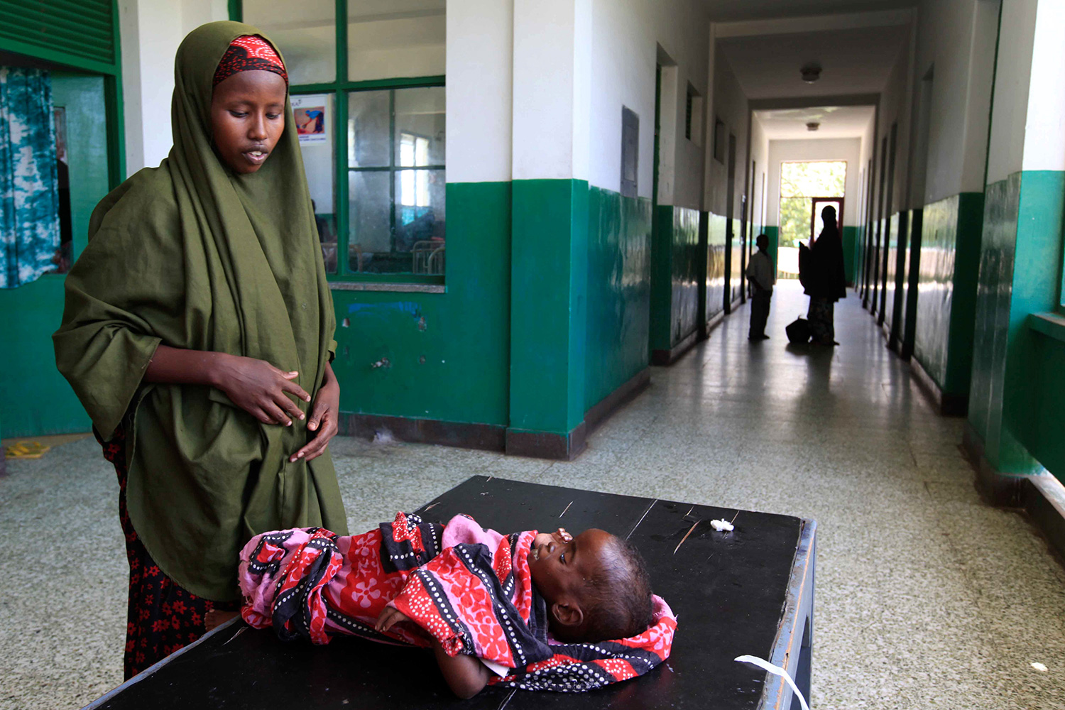 The photo shows the woman standing over her baby, who shows signs of malnourishment and is lying on a table.