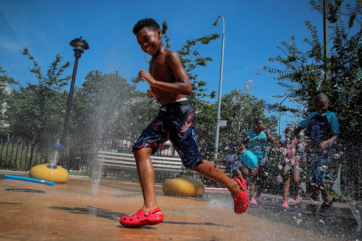 The photo shows several children running gleefully through spraying sprinklers.