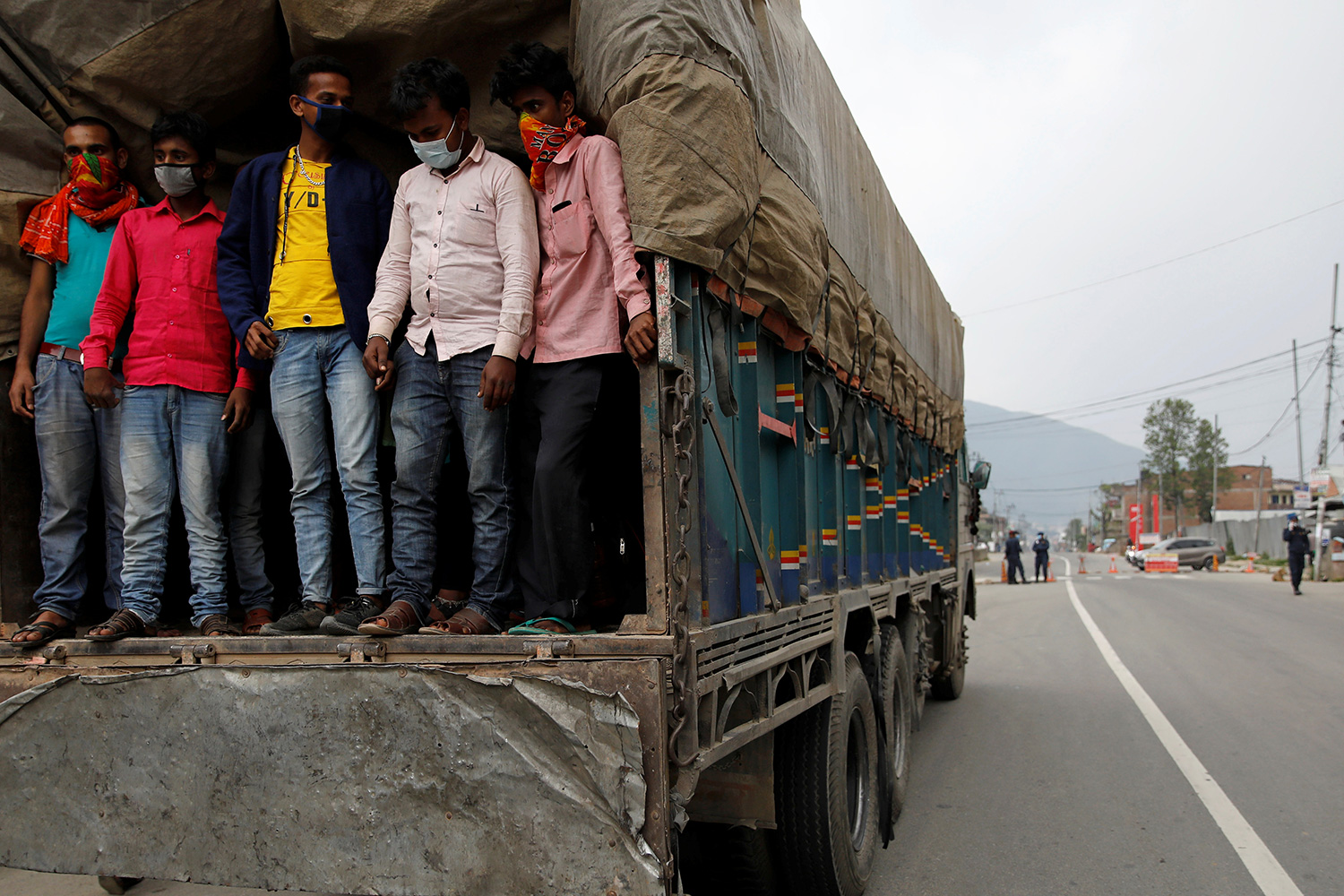 The photo shows a large flatbed trick covered with sides and a green tarp on a road. standing in the back of the truck can be seen several men.
