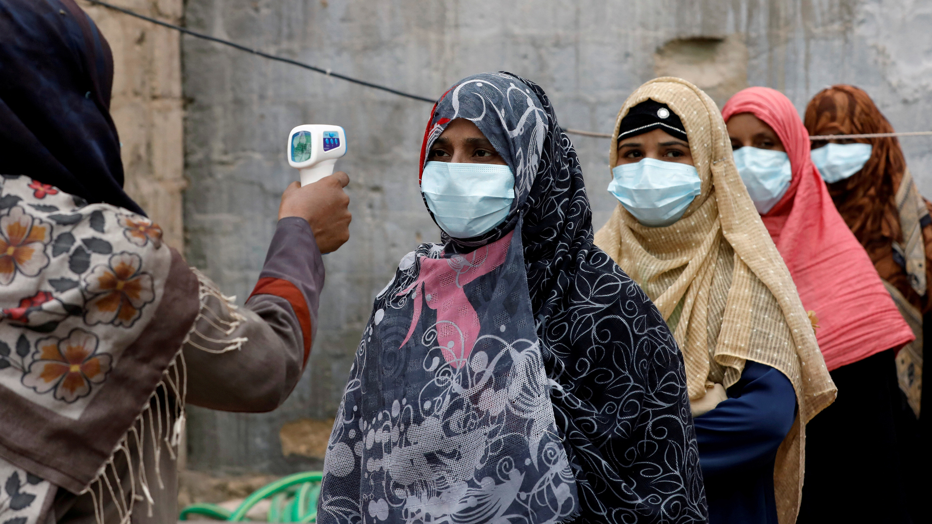 The photo shows several people lined up while their temperature is being checked.