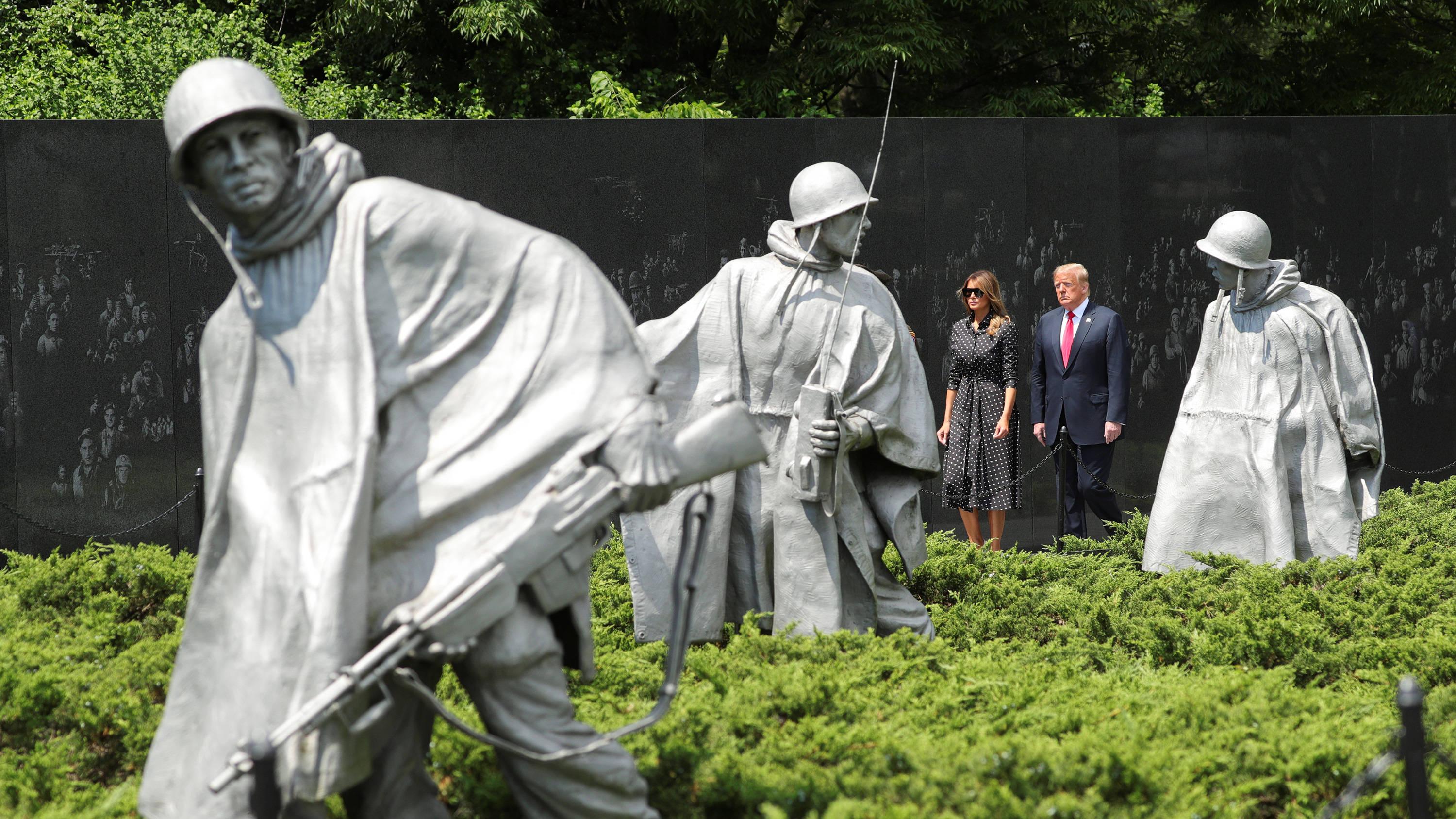 The photo shows the president and first lady shot from across the monument with statues of 1950s soldiers seen in the foreground.