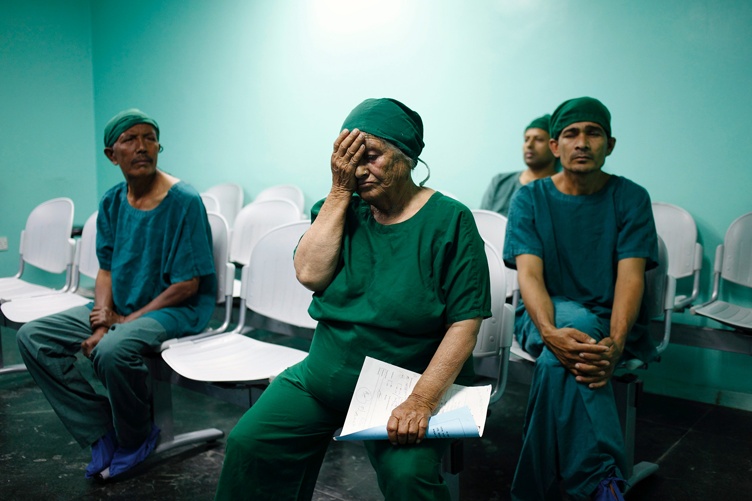 Picture shows several people wearing green scrubs—with a woman in front holding a hand over her face.