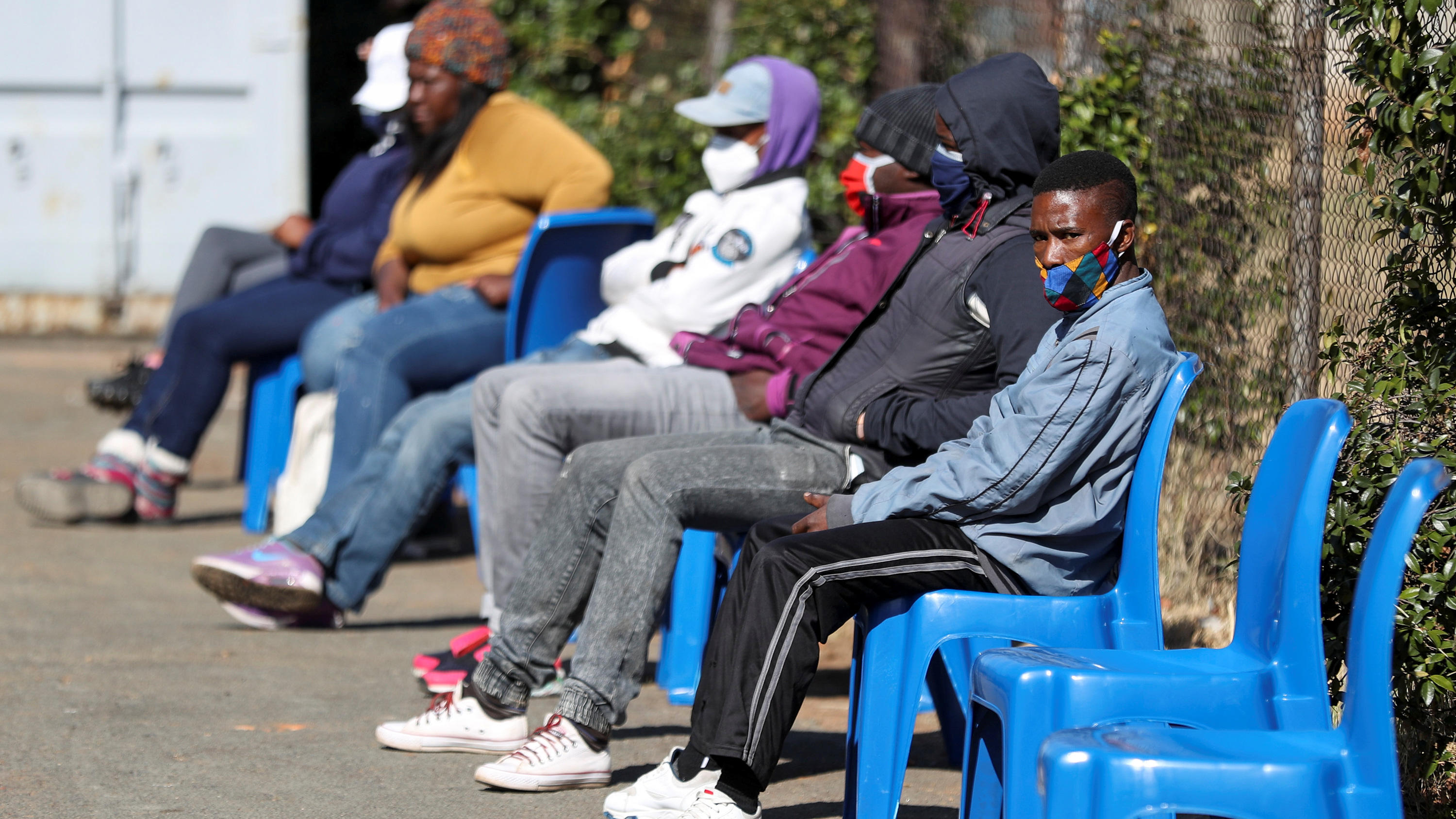 The photo shows a line of people waiting outside in chairs.