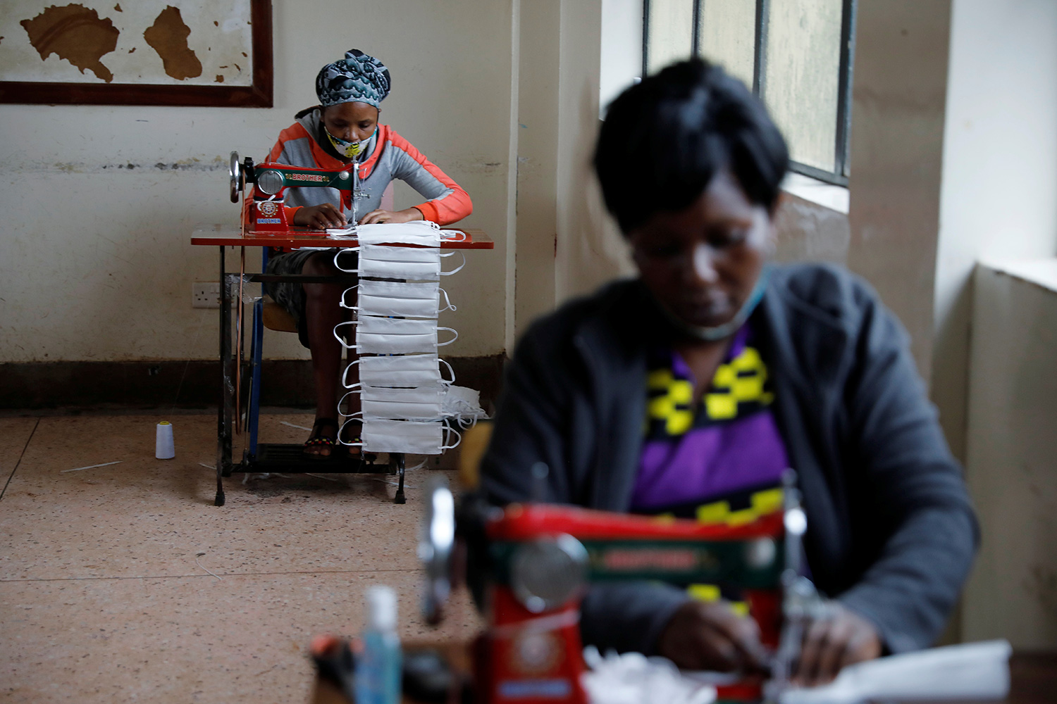 The photo shows two woman at sewing machines finishing strings of masks.