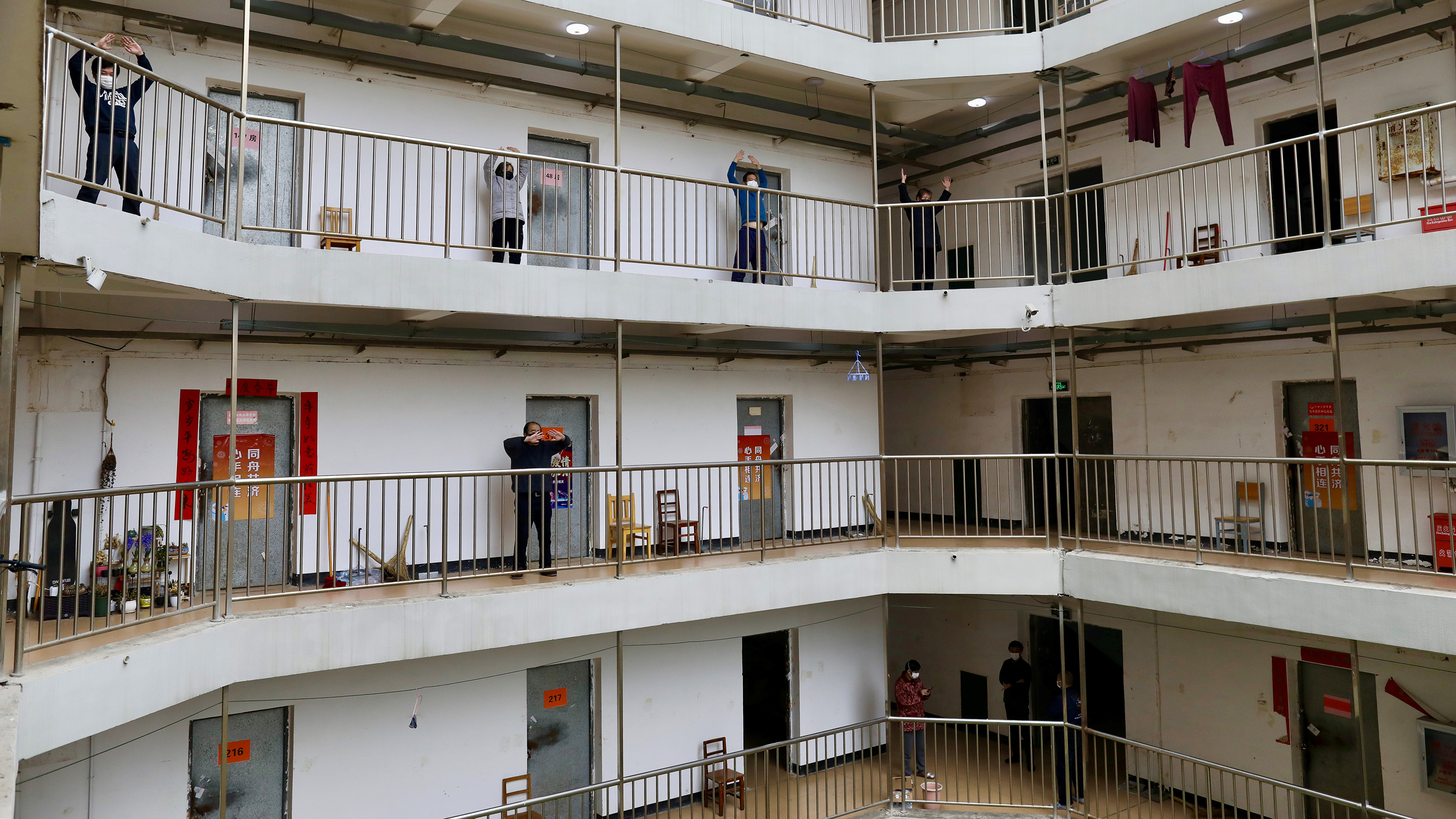 The photo shows multiple levels of an apartment building-type structure with several people on one of the floors exercising in the open-air walkway.
