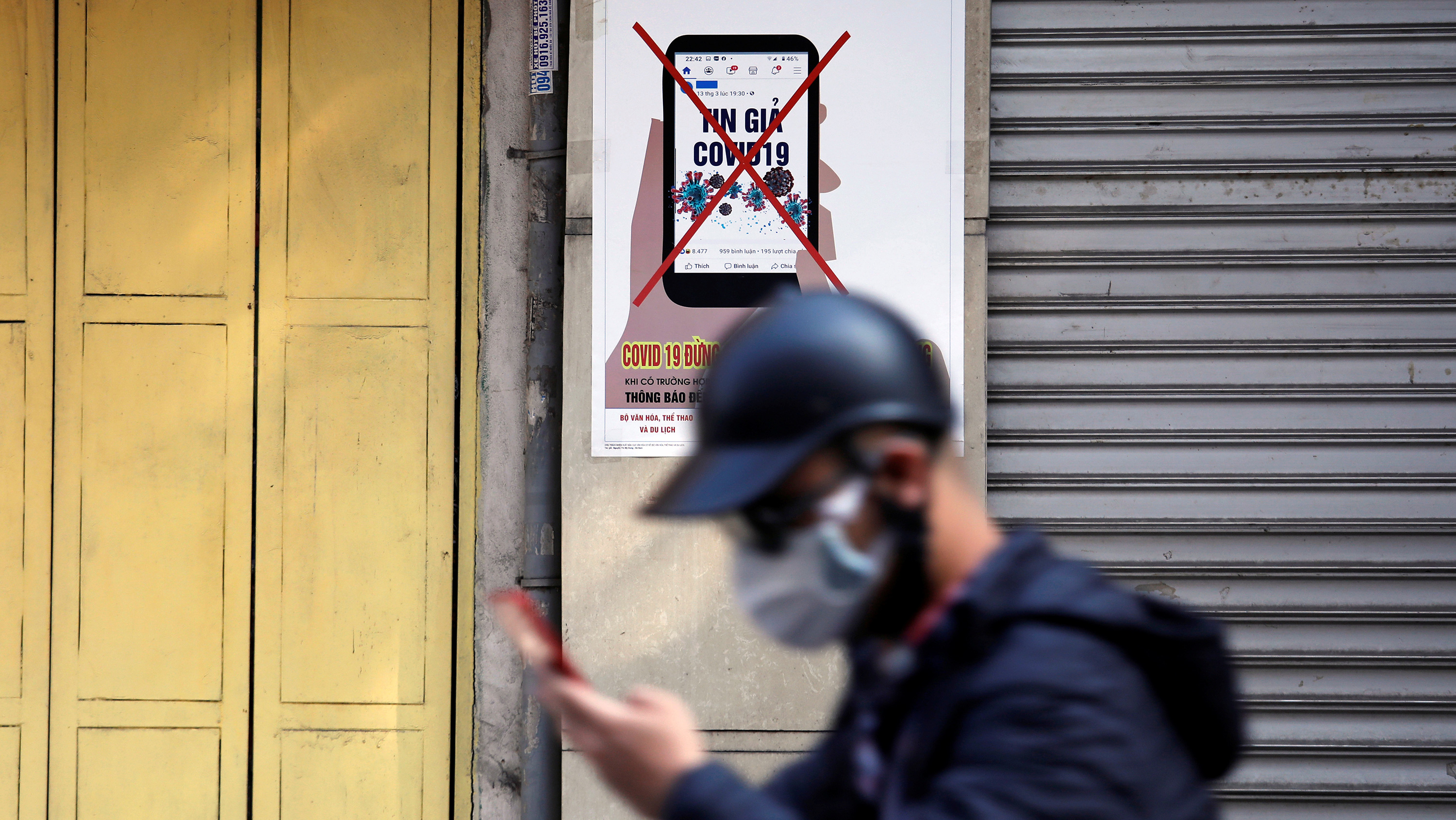 Picture shows a man with a hat walking out of focus in the foreground against a PSA picture posted on a wall.