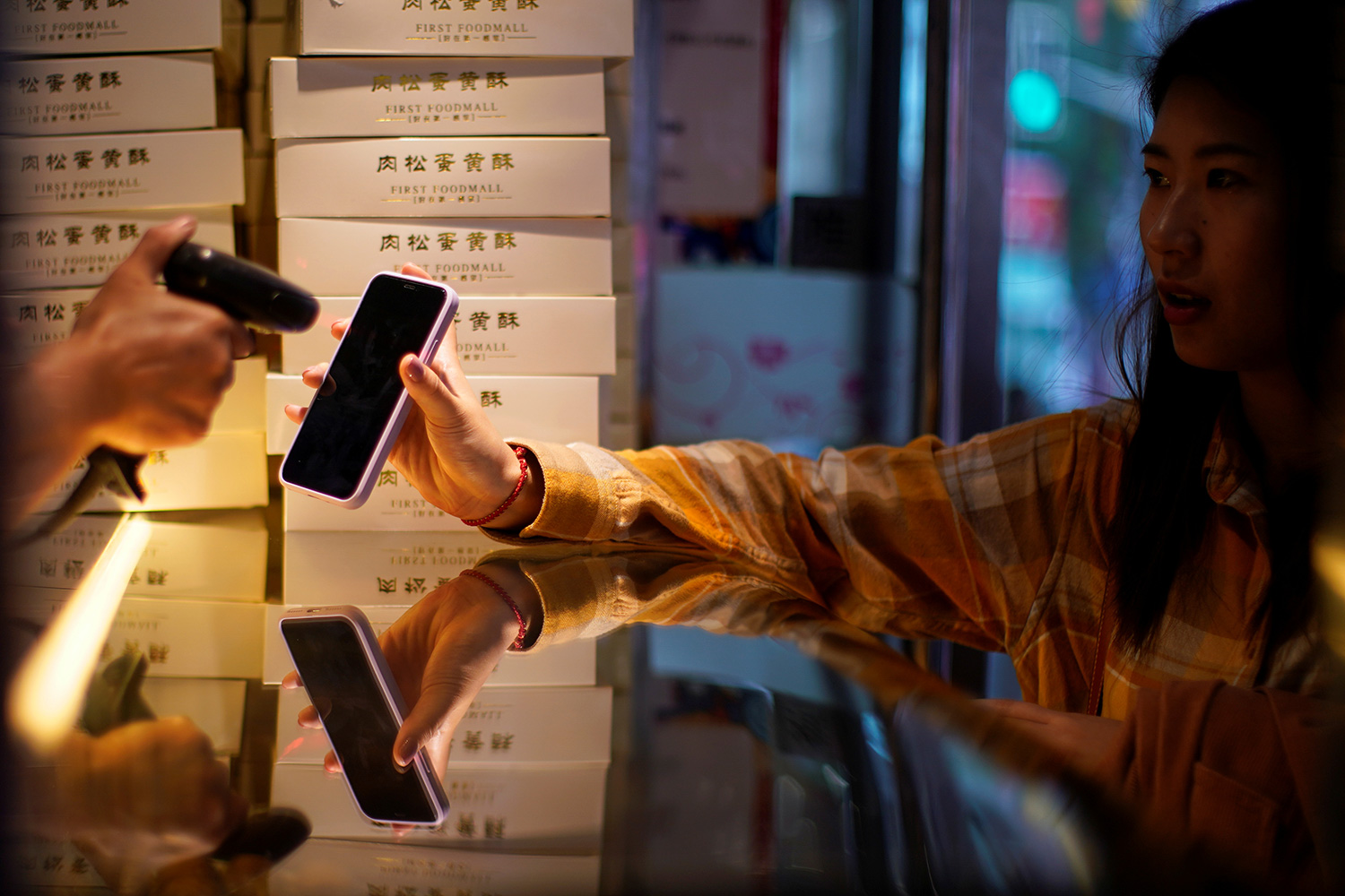 The photo shows a woman holding her phone up for the teller to scan amid mask wearing and other protective measures.