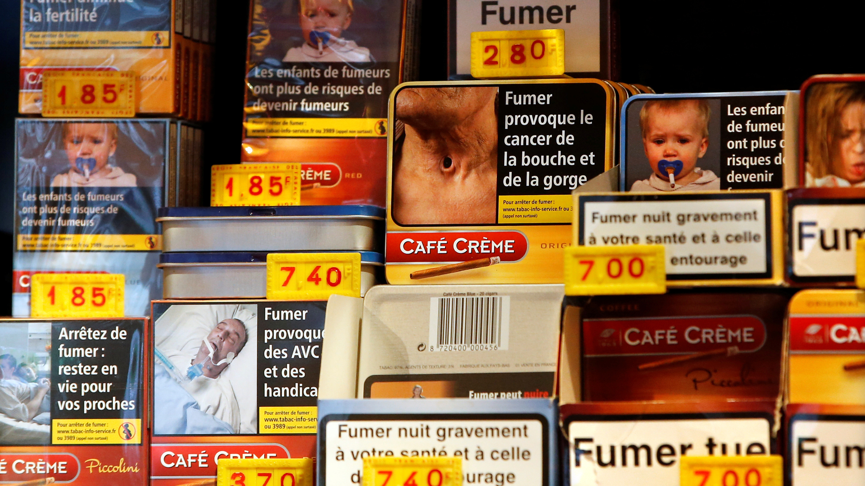 The image shows a tobacco store shelf with a variety of boxes all adorned with graphic warming labels.