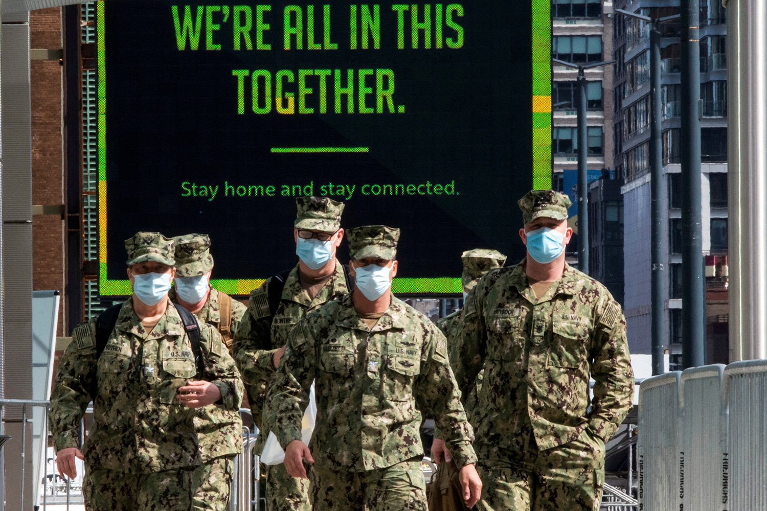 The photo shows a group of soldiers in fatigues walking toward the camera with a sign seen in the background that reads, "WE'RE ALL IN THIS TOGETHER."