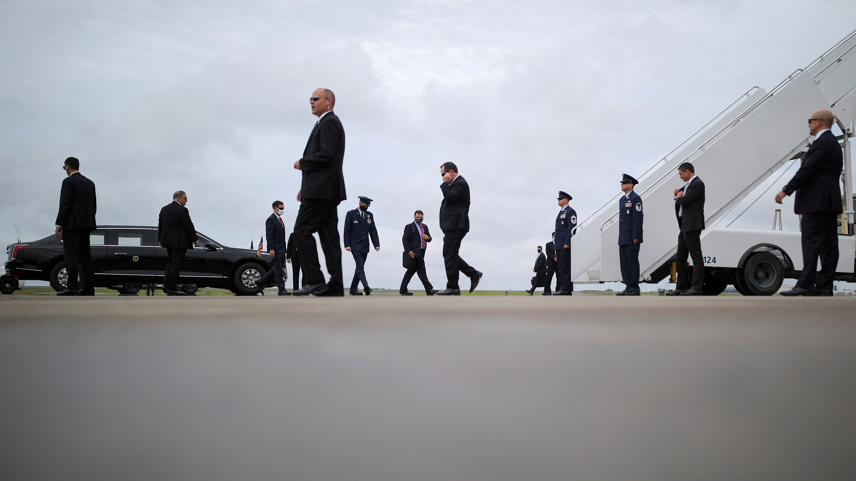 The photo shows a plane on the tarmac as well as a limosine from a distance with lots of people in suits walking about.