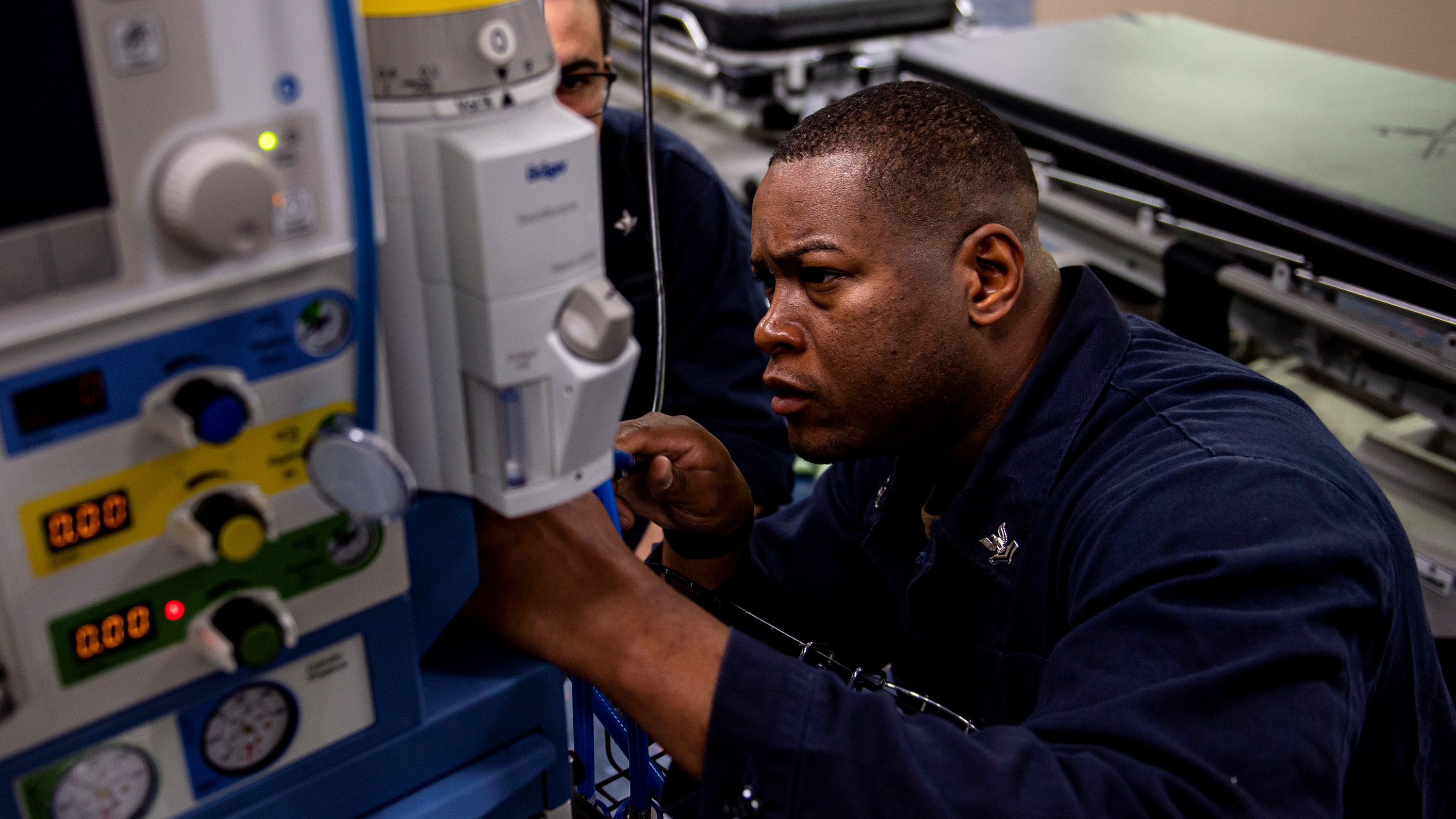 Picture shows the corpsman kneeling slightly while he works on a machine.