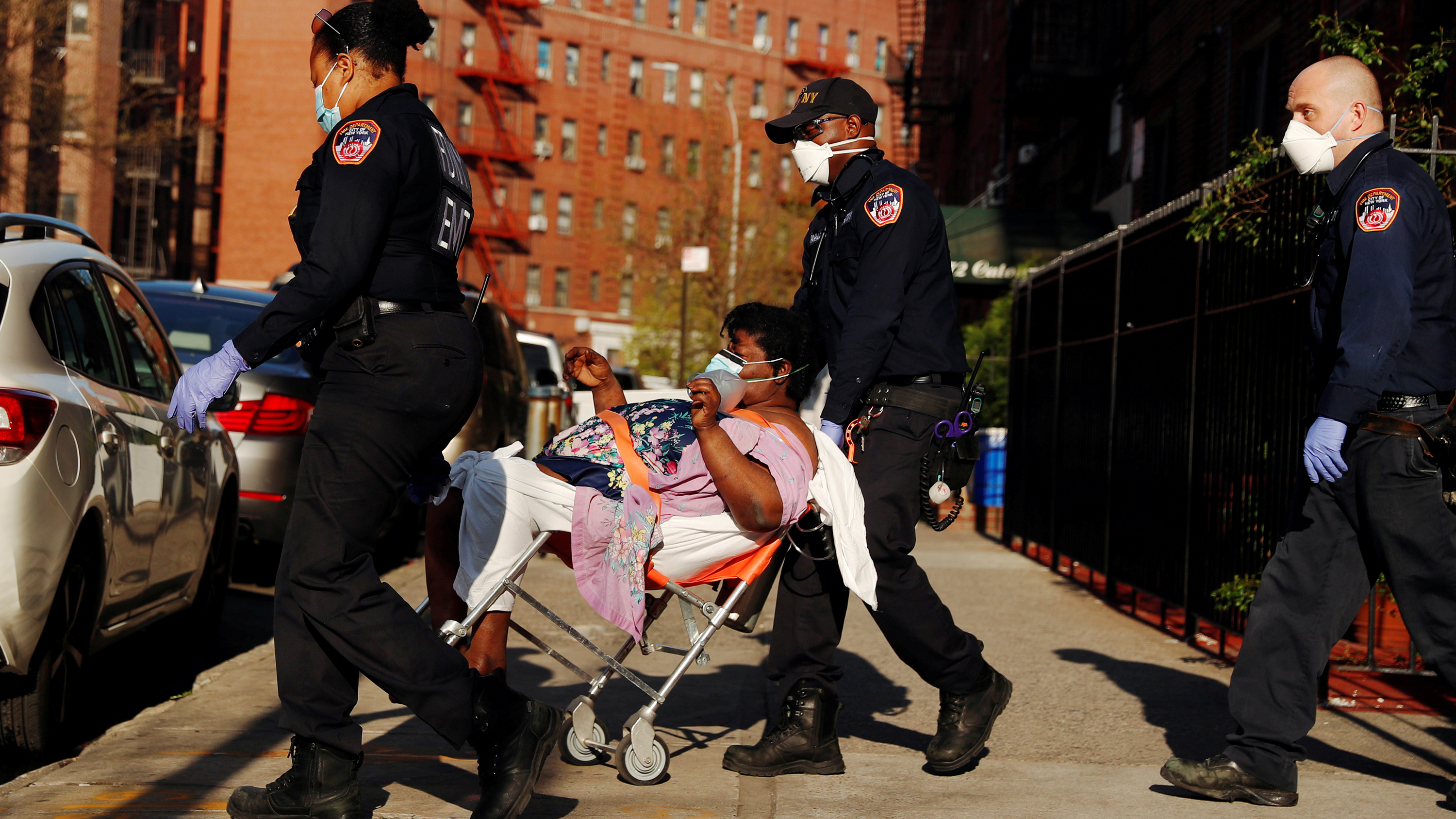 The photo shows three EMTs wheeling a gurney with a woman on a clear day in some part of the city.