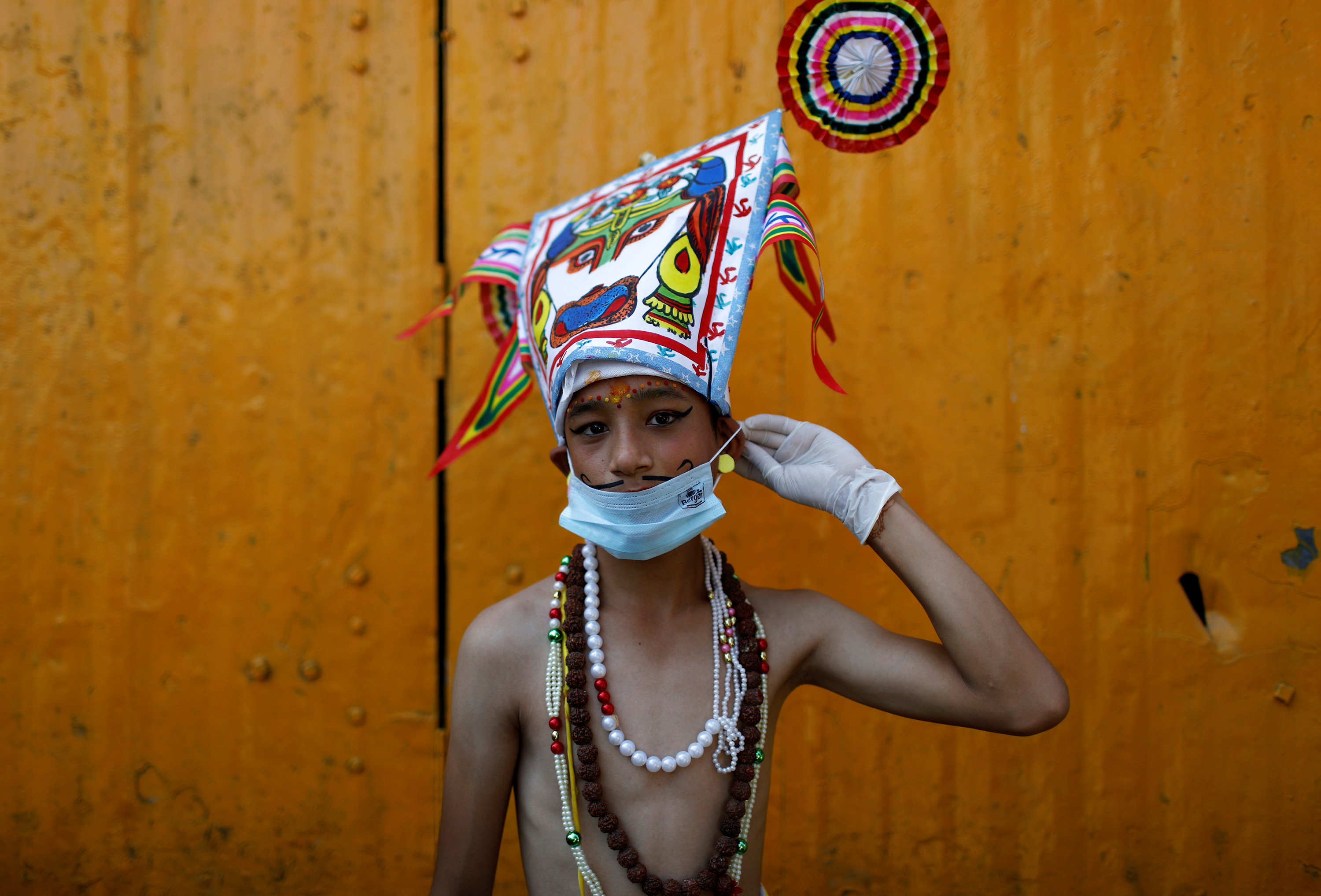 The photo shows a boy in a colorful costume and a surgical facemask during a festival in which people ask for salvation and peace for their departed loved ones.