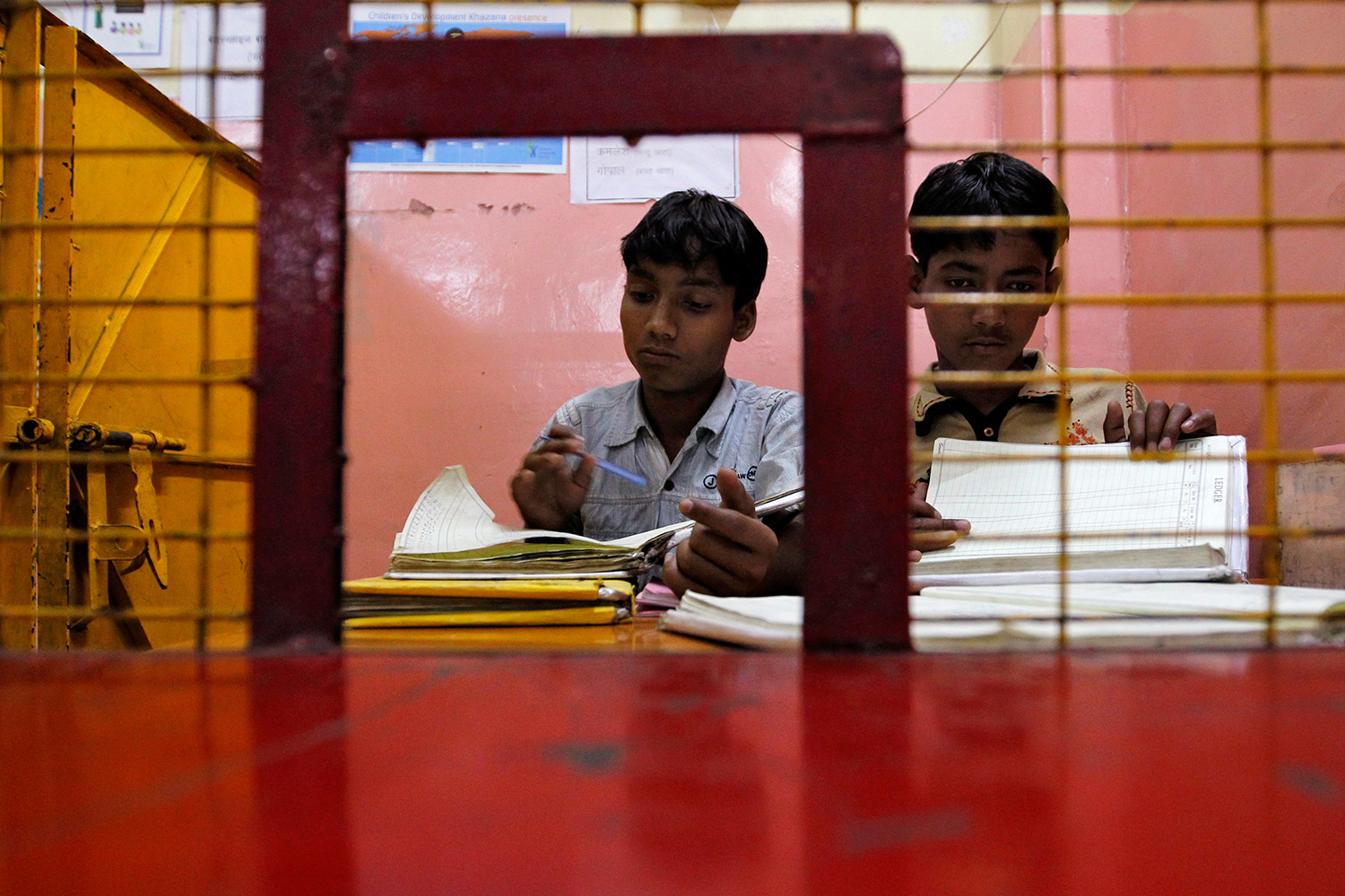 The photo shows two children behind a cashier's window looking through stacks of paper.