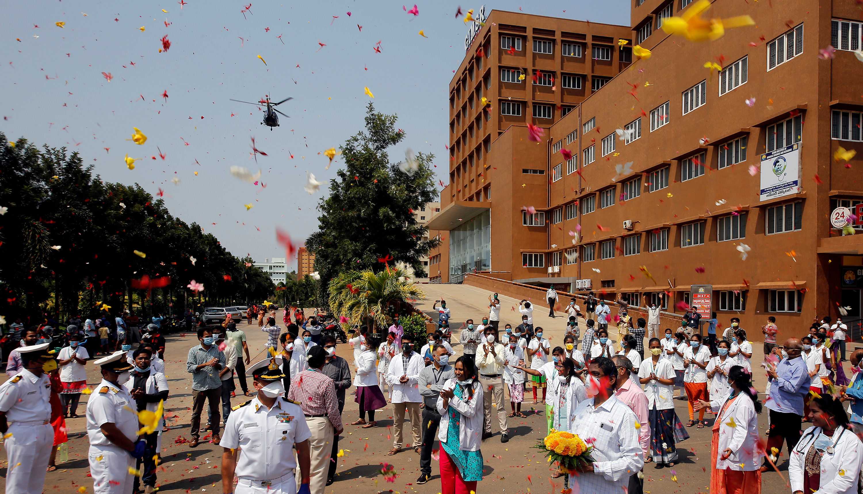 The photo shows a large brick hospital with lots of health workers and some uniformed naval officers out front as a shower of flower pedals rains down on them from above.