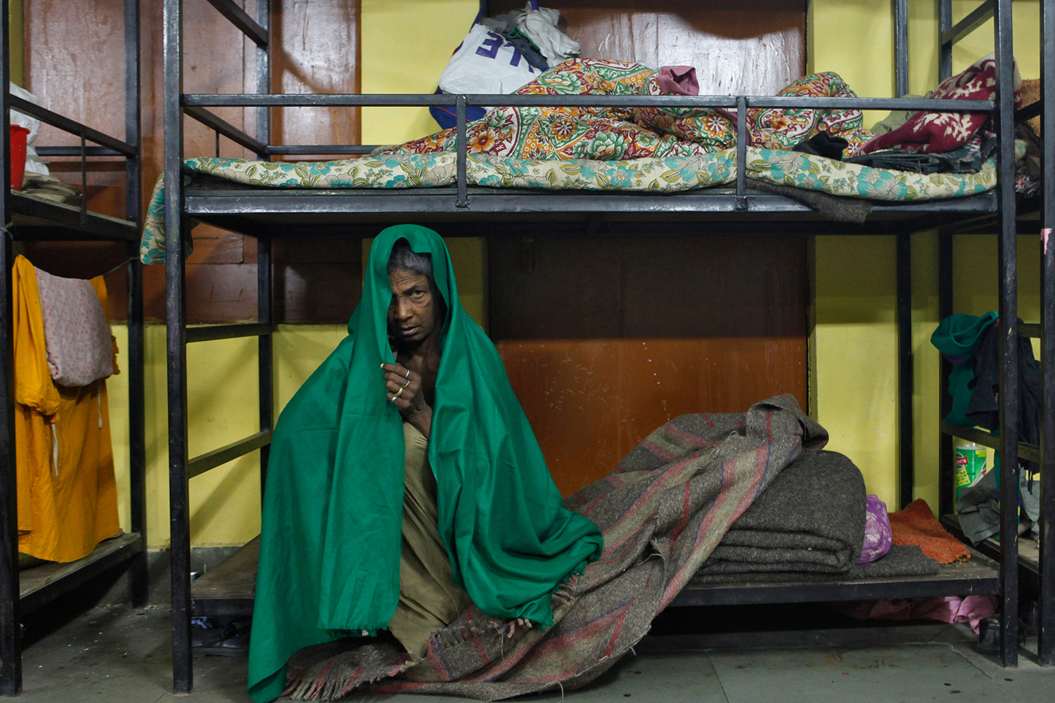 Picture shows a woman sitting on a bunk while wrapped in a bright green blanket.