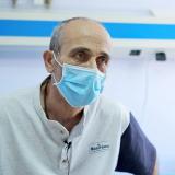 A middle-aged man wearing a light-blue surgical mask sits in a doctor's office. 