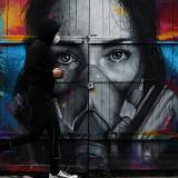 A man wearing a face mask jogs by street art in Brick Lane, in London, on April 18, 2020.