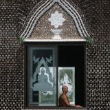 A Buddhist monk looks out of the window of the Wat Pa Maha Chedi Kaew temple, built with more than a million glass bottles