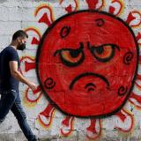 A Palestinian man walks past cartoon-style street art of the novel coronavirus SARS-CoV-2, with its signature spike proteins, in Gaza City, on October 4, 2020.