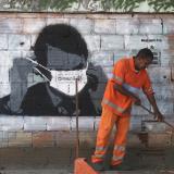 A municipal worker cleans a street in front of street art depicting Brazilian President Jair Bolsonaro adjusting his face mask during the COVID-19 outbreak in Rio de Janeiro, Brazil, on March 26, 2020.