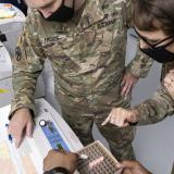 Two U.S. soldiers in green uniforms examine vials of vaccine material and data.