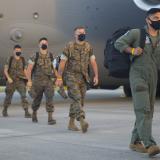 Four uniformed U.S. Marines file out of a grey personnel carrier aircraft.