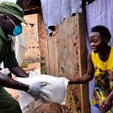 A Ugandan soldier in a green uniform gives a bag a food to a young woman in a yellow dress.
