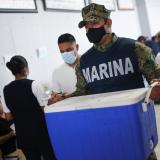 A soldier in a navy blue Marine Corps vest carries a blue cooler of vaccines through an active vaccination site.