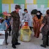 A soldier directs women in colorful dresses and headscarves in a classroom that doubles as a vaccination site.