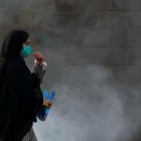 A woman wearing a protective mask walks past a cloud of smoke from a smoldering pile of rubbish along a road in Karachi, Pakistan, on October 13, 2021. 