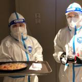 Two hotel staff wearing personal protective equipment (PPE) deliver a Margherita pizza wrapped in cling film that was ordered with room service at a hotel for journalists and officials o